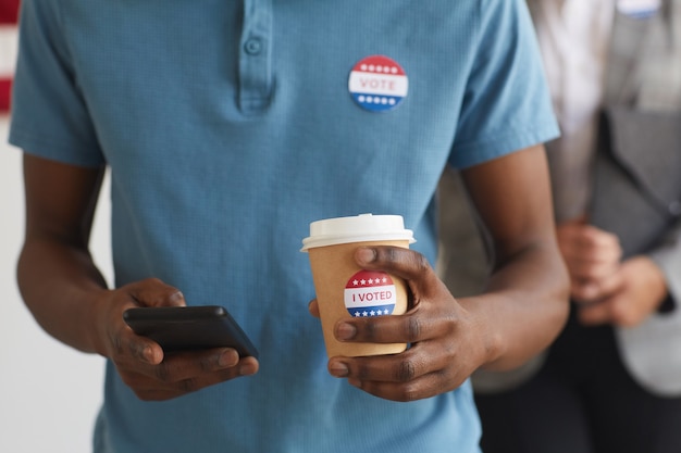 Retrato de seção intermediária de um jovem afro-americano com o adesivo "VOTEI" em pé na seção eleitoral no dia da eleição