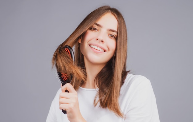 Retrato de senhora de cabelo morena sorridente, penteando o cabelo com pente de escova de cabelo isolado Jovem mulher bonita...