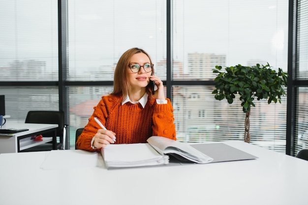 Retrato de senhora feliz digitando no celular enquanto está na mesa do escritório