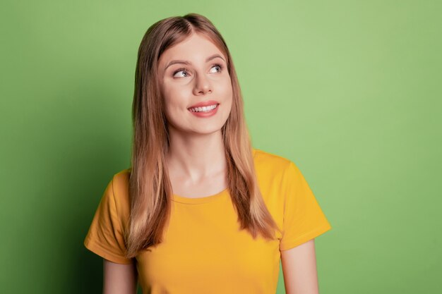 Retrato de senhora inspirada, sorriso branco, olhar para o espaço vazio, usar uma camiseta amarela isolada no fundo de cor verde