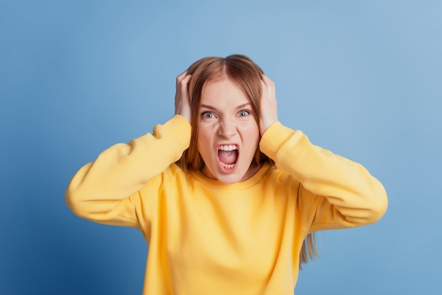 Retrato de senhora irritada e indignada a rasgar o cabelo da câmera de olhar alto sobre fundo azul