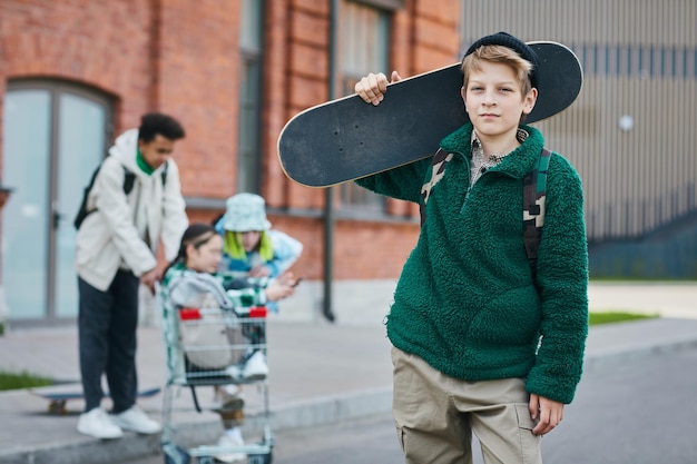 Foto retrato de skatista segurando seu skate e olhando para a câmera em pé na rua com fr