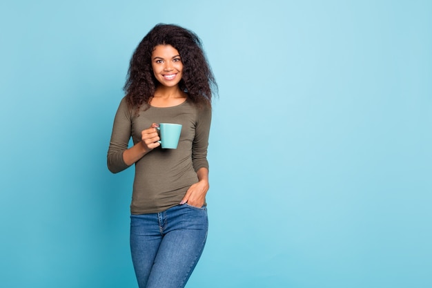 Retrato de sonho sonhador positivo alegre mulata segurando xícara com café expresso cacau sentir conteúdo usar roupas estilo casual jeans isolado sobre parede de cor azul