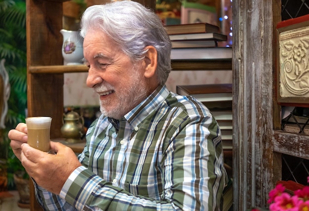 Retrato de sorridente avô barbudo dos anos 70 sentado segurando uma xícara de café com leite homem idoso feliz relaxando aproveitando a pausa com cappuccino quente