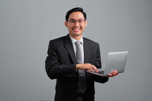 Retrato de sorridente jovem empresário bonito em terno formal segurando um laptop aberto na mão isolado em fundo cinza