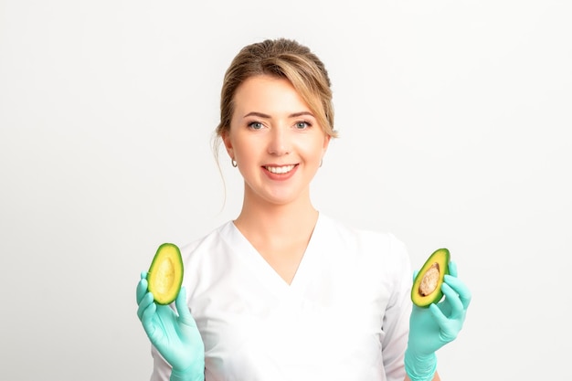 Retrato de sorridente jovem nutricionista médica com frutas orgânicas de abacate posando para a câmera no espaço de cópia de fundo branco Benefícios da nutrição adequada