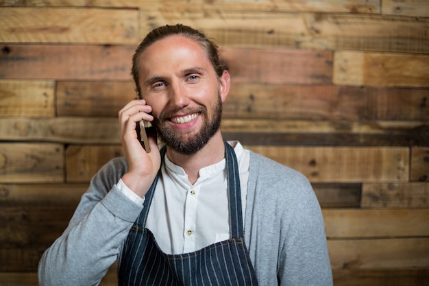 Retrato, de, sorrindo, garçom, falando telefone móvel, contra, parede madeira