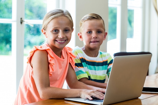 Retrato, de, sorrindo, irmãos, usando computador portátil, tabela