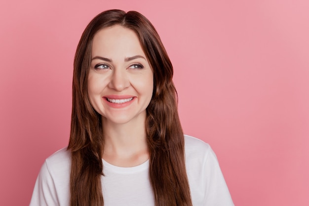 Retrato de sorriso brilhante de menina curiosa e positiva parece um espaço vazio no fundo rosa