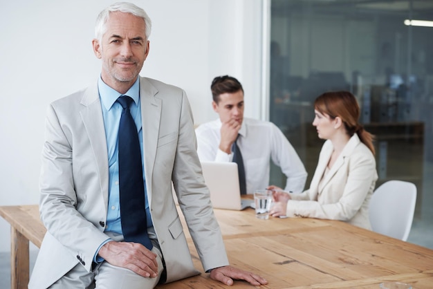 Retrato de sorriso e homem de negócios na mesa na sala de reuniões do escritório para planejamento ou gerenciamento de reuniões Treinamento ou educação de liderança com gerente maduro confiante no local de trabalho para o crescimento dos funcionários