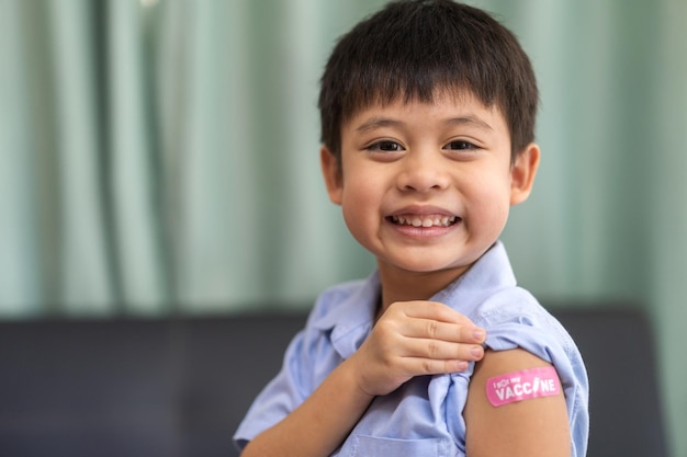 Retrato de sorriso feliz vacinado garotinho asiático crianças de 5 a 11 anos de idade posando mostrar o braço com gesso médico após a vacina de injeção Proteção Covid19 criança vacinação contra o vírus