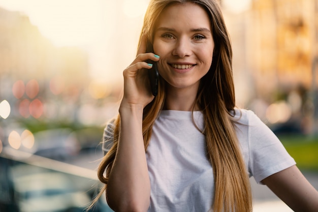 Retrato de sorriso novo atrativo da mulher que fala ao ar livre no telefone. Imagem de estilo de vida.