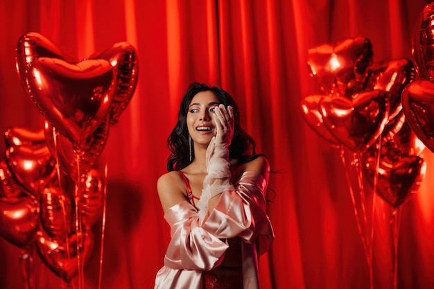 Retrato de sorriso sexy menina asiática maquiagem glam em lingerie e luvas de renda entre balões vermelhos brilhantes