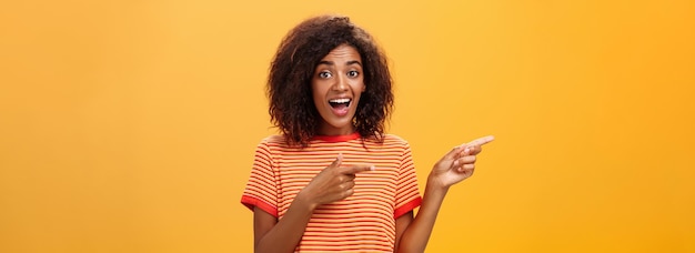 Foto retrato de surpreendida, animada, carismática, de pele escura, jovem e bonita, com penteado afro de moda.