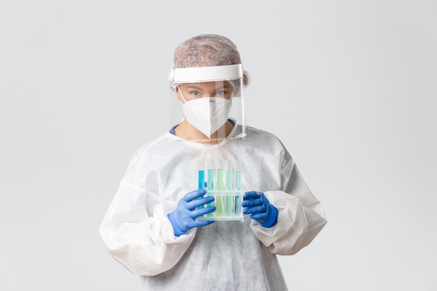 Retrato de técnico de laboratório, cientista ou médico em equipamento de proteção individual segurando tubos de ensaio com amostras de vacina, em busca da cura.