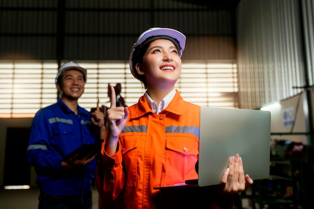 Retrato de técnico feminino masculino engenheiro asiático em uniforme de segurança em pé e se virar para olhar para a câmera e rir com sorriso alegre e confiante no fundo do local de trabalho da fábrica de máquinas