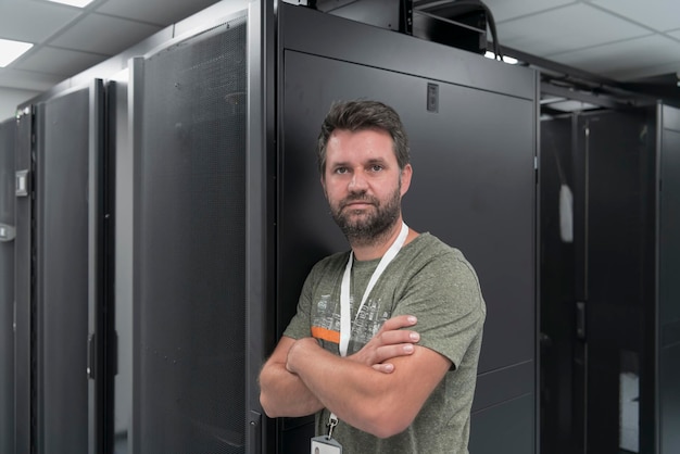 Retrato de técnico masculino ou administrador de rede corajoso como um herói com os braços cruzados na sala do servidor do data center. Foto de alta qualidade