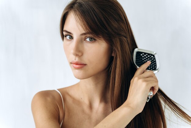 Retrato de tiro na cabeça 25s mulher alegre segurando a escova de cabelo e arrumar seu cabelo forte e saudável depois de tomar um banho. Estilo de vida de rotina de beleza matinal, publicidade de tratamento para o crescimento perfeito do cabelo, cuidados com os cabelos