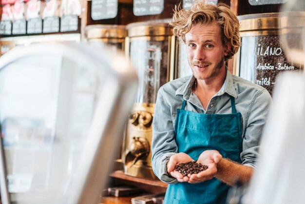 Retrato de torrador de café em sua loja segurando grãos de café