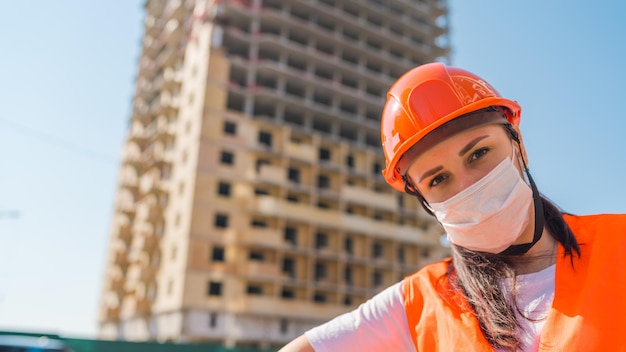 Retrato de trabalhador da construção civil em máscara médica e macacão no fundo da casa em construção