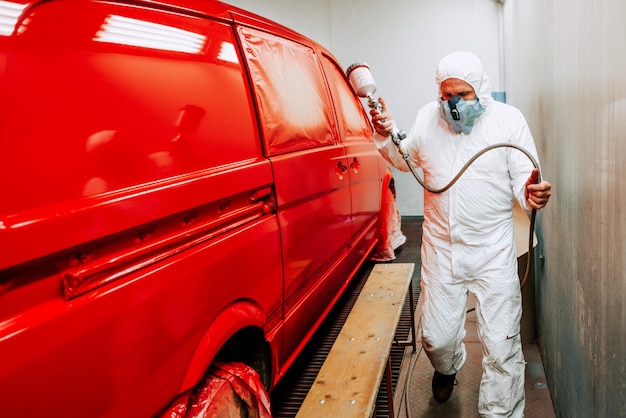 Foto retrato de trabalhador mecânico de automóveis pintando um carro van vermelho