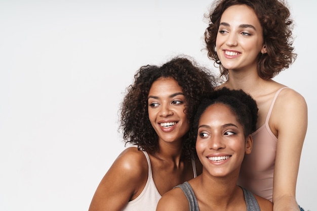 Retrato de três alegres mulheres multirraciais sorrindo e olhando para o lado