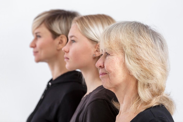 Retrato de três gerações de mulheres loiras em uma família Mãe séria avó e neta em camisolas pretas estão umas atrás das outras Foco seletivo Fundo branco