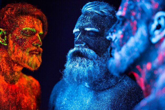 Retrato de três homens barbudos pintados em pó fluorescente.