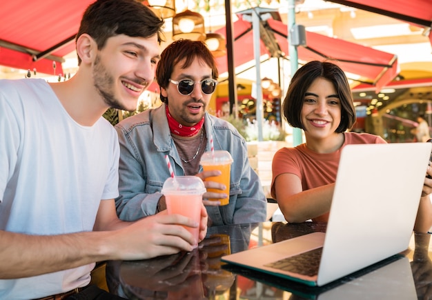 Retrato de três jovens amigos usando um laptop enquanto está sentado ao ar livre no café. Conceito de amizade e tecnologia.