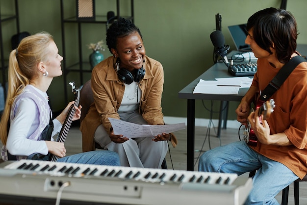 Retrato de três jovens músicos escrevendo músicas juntos focam na mulher negra sorrindo alegremente e ho