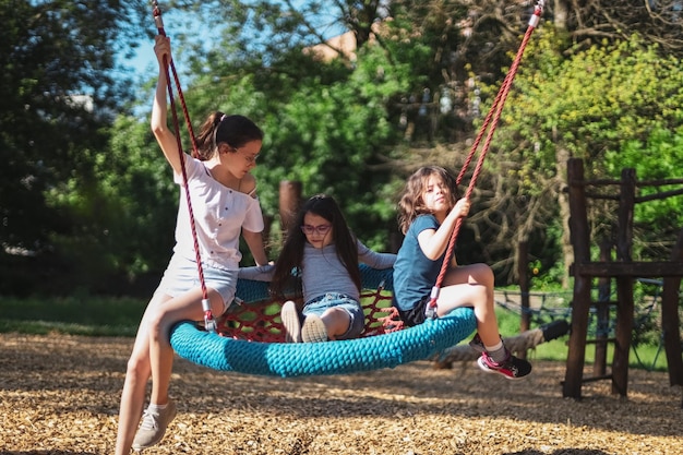 Retrato de três lindas garotas caucasianas, irmãs, andam juntas em um balanço de corda redonda no parque
