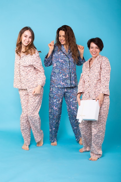Retrato de três lindas garotas de pijama colorido se divertindo durante a festa do pijama