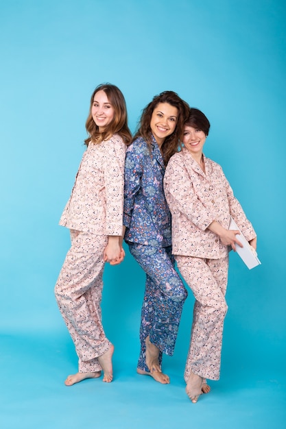 Retrato de três lindas garotas de pijama colorido se divertindo durante a festa do pijama