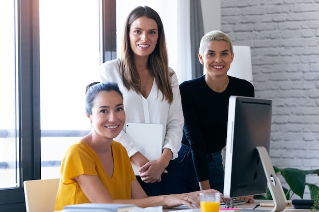 Retrato de três mulheres empreendedoras modernas, olhando para a câmera enquanto trabalhava no escritório.