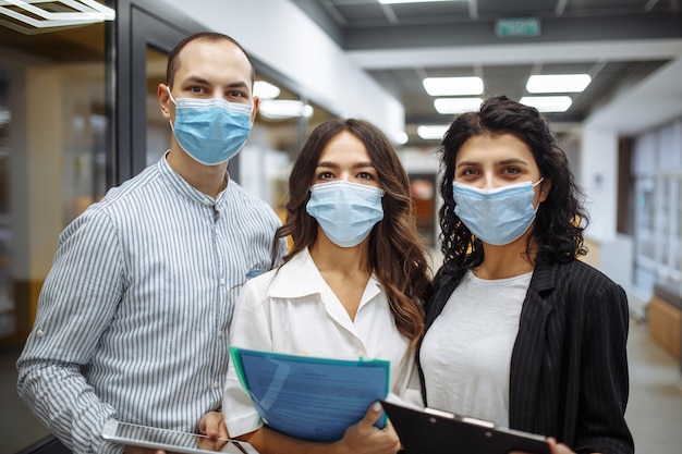 Foto retrato de três trabalhadores de escritório usando máscaras médicas, discutindo negócios e perspectivas futuras.