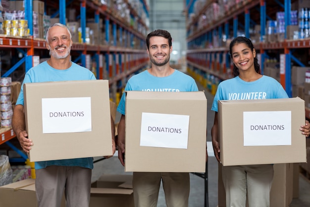 Retrato de três voluntários segurando uma caixa de doações