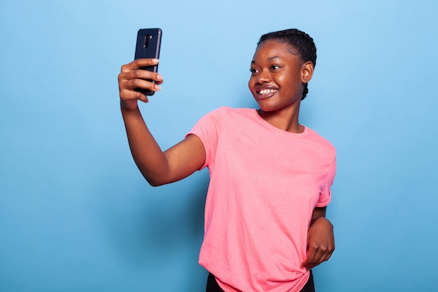 Retrato de um adolescente afro-americano alegre segurando um telefone, tirando foto