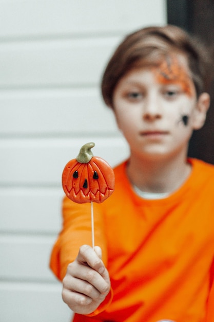 Retrato de um adolescente autêntico sincero com rosto pintado na festa de Halloween com Jack pirulito
