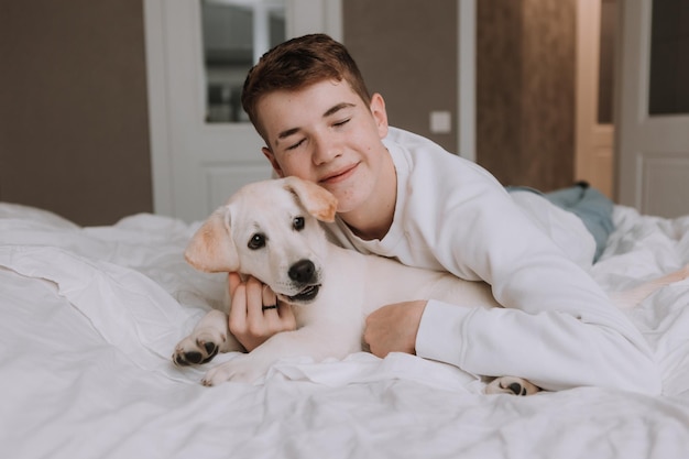 Retrato de um adolescente deitado na cama na cama branca em um abraço com um cachorro de cor clara