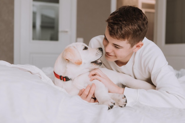 Retrato de um adolescente deitado na cama na cama branca em um abraço com um cachorro de cor clara