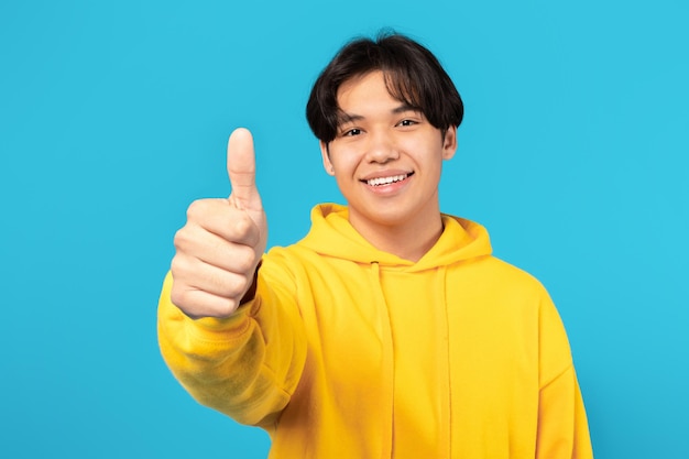 Retrato de um adolescente japonês gesticulando com os polegares para cima fundo azul