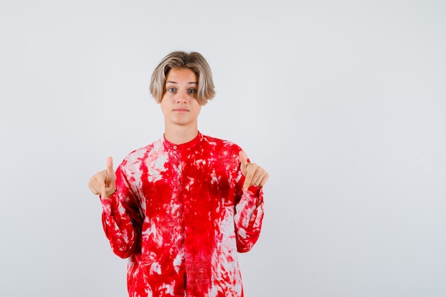 Retrato de um adolescente loiro apontando para baixo com uma camisa grande e olhando a vista frontal sem graça