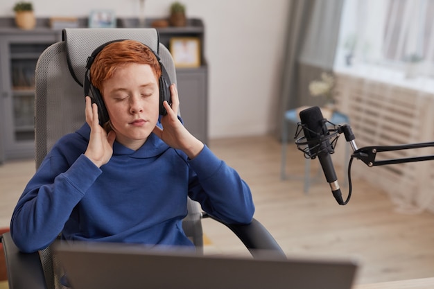 Retrato de um adolescente ruivo usando fones de ouvido e curtindo música com os olhos fechados enquanto relaxa ou grava um podcast, copie o espaço