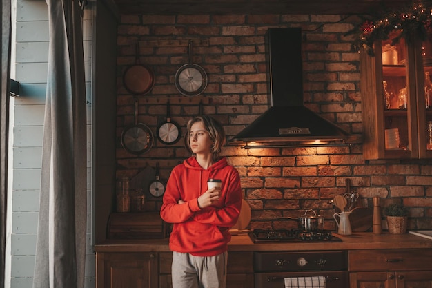 Retrato de um adolescente sincero e autêntico cozinhando na cozinha em um chalé de madeira decorado para o Natal