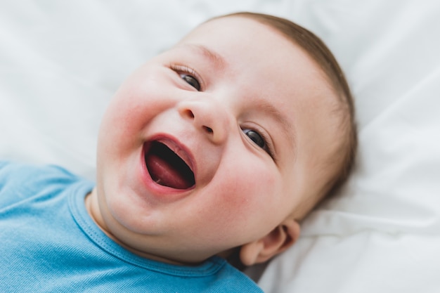 Retrato de um adorável bebê de 3 meses sorrindo, deitado em uma cama de lençóis brancos