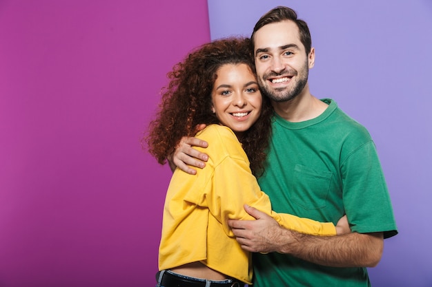 Retrato de um alegre casal caucasiano, homem e mulher com roupas coloridas, sorrindo e se abraçando isolados