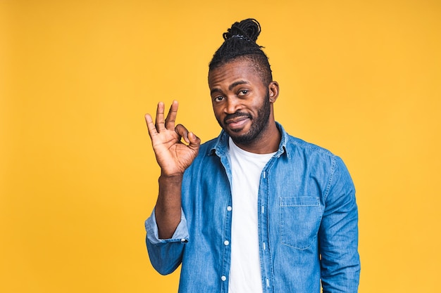 Retrato de um alegre feliz sorridente jovem negro afro-americano em pé isolado sobre fundo amarelo. Ok, sinal.