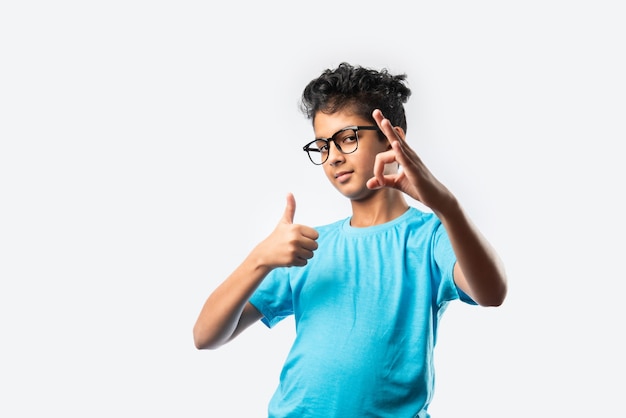 Retrato de um alegre garotinho indiano asiático com óculos celebrando o sucesso em pé contra uma parede branca