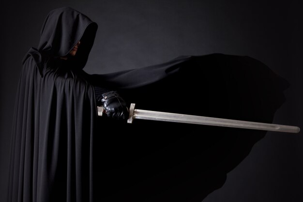 Retrato de um andarilho guerreiro corajoso em uma capa preta e espada na mão.