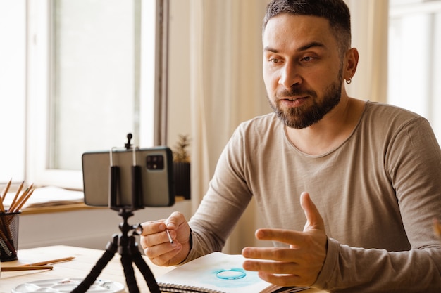 Retrato de um artista de midadult homem de cabelos escuros sorrindo feliz fazendo aula de arte online para alunos